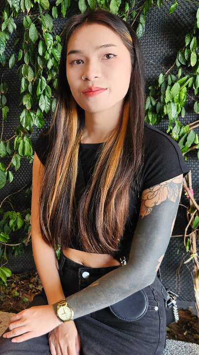 Slender tattooed TukTuk Patrol Rain sits near vines